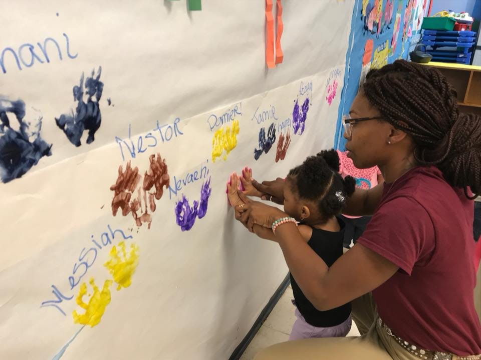 Person helping a child make a handprint on a wall with other handprints