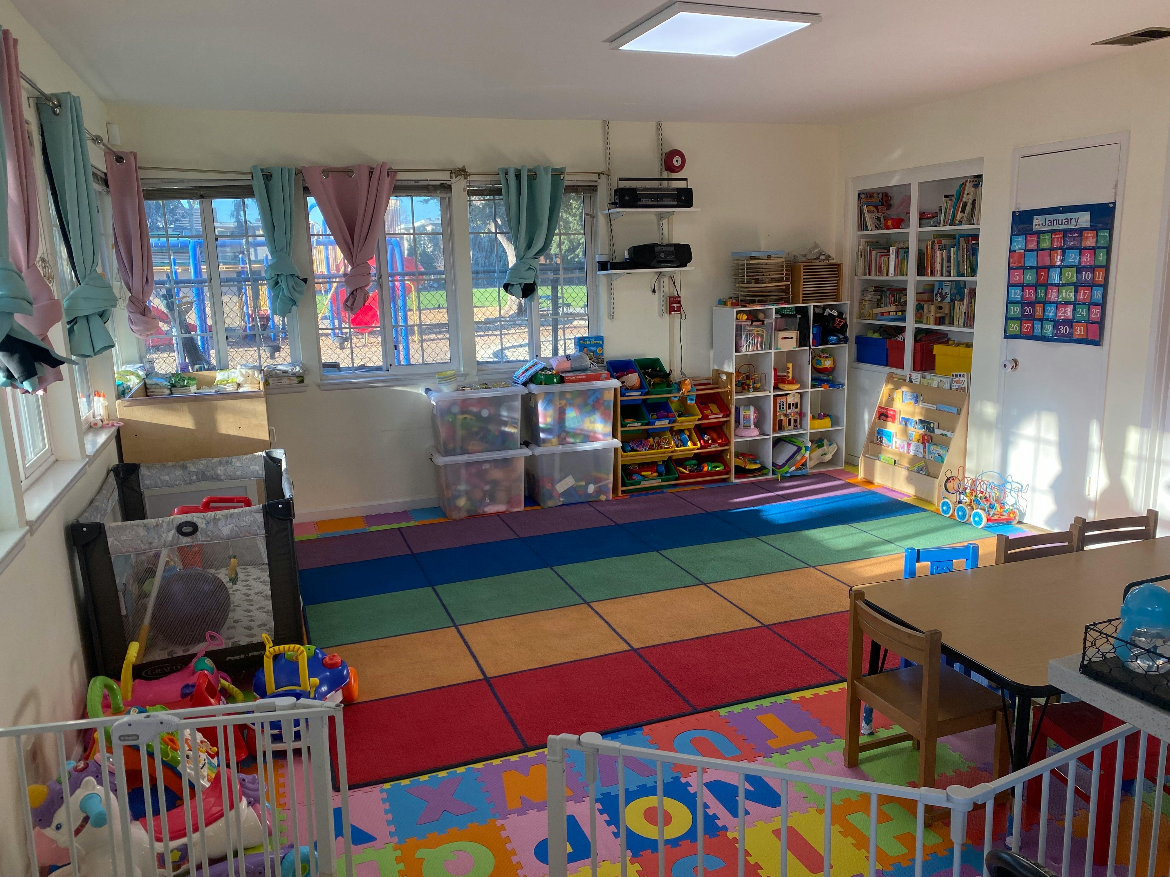 A colorful playroom with a rainbow-colored floor, cribs, and a small table with chairs