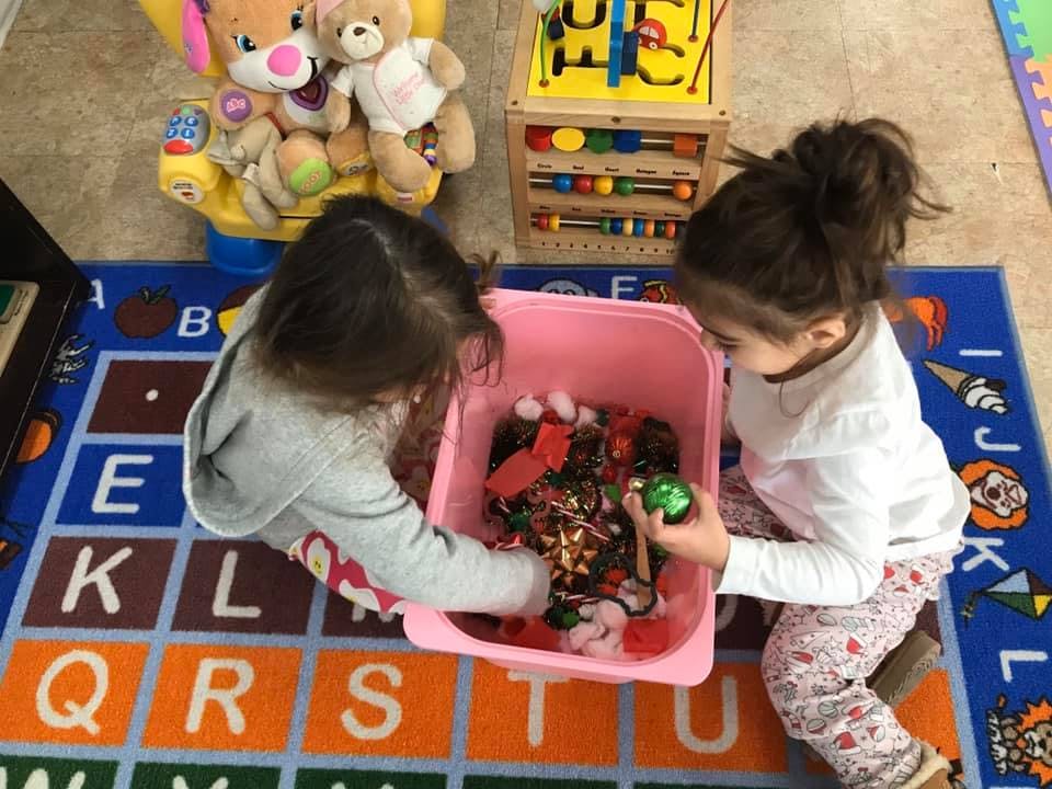 Two children playing with items in a pink bin on an alphabet rug