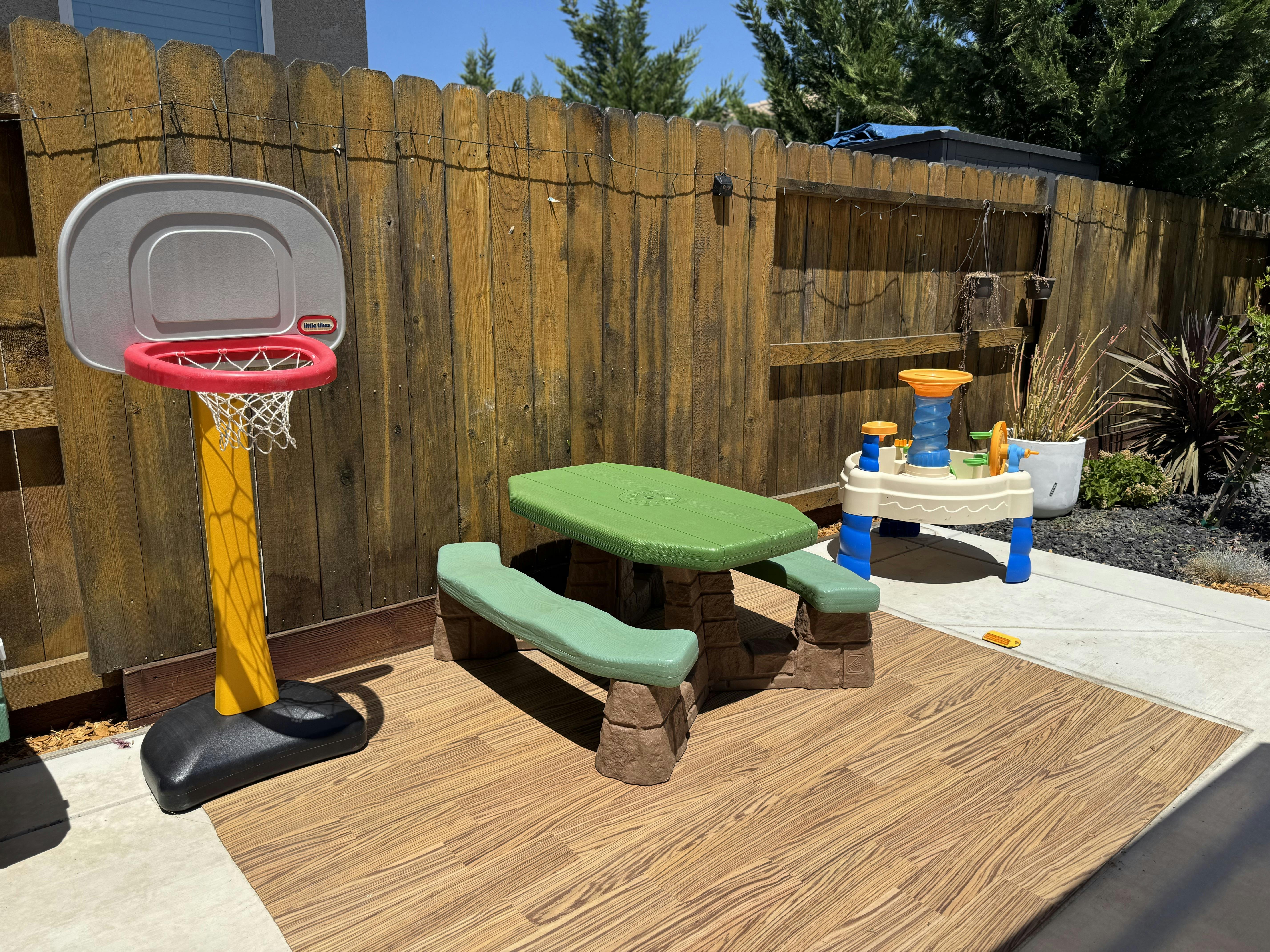 Children's basketball hoop, picnic table, and water table in a backyard