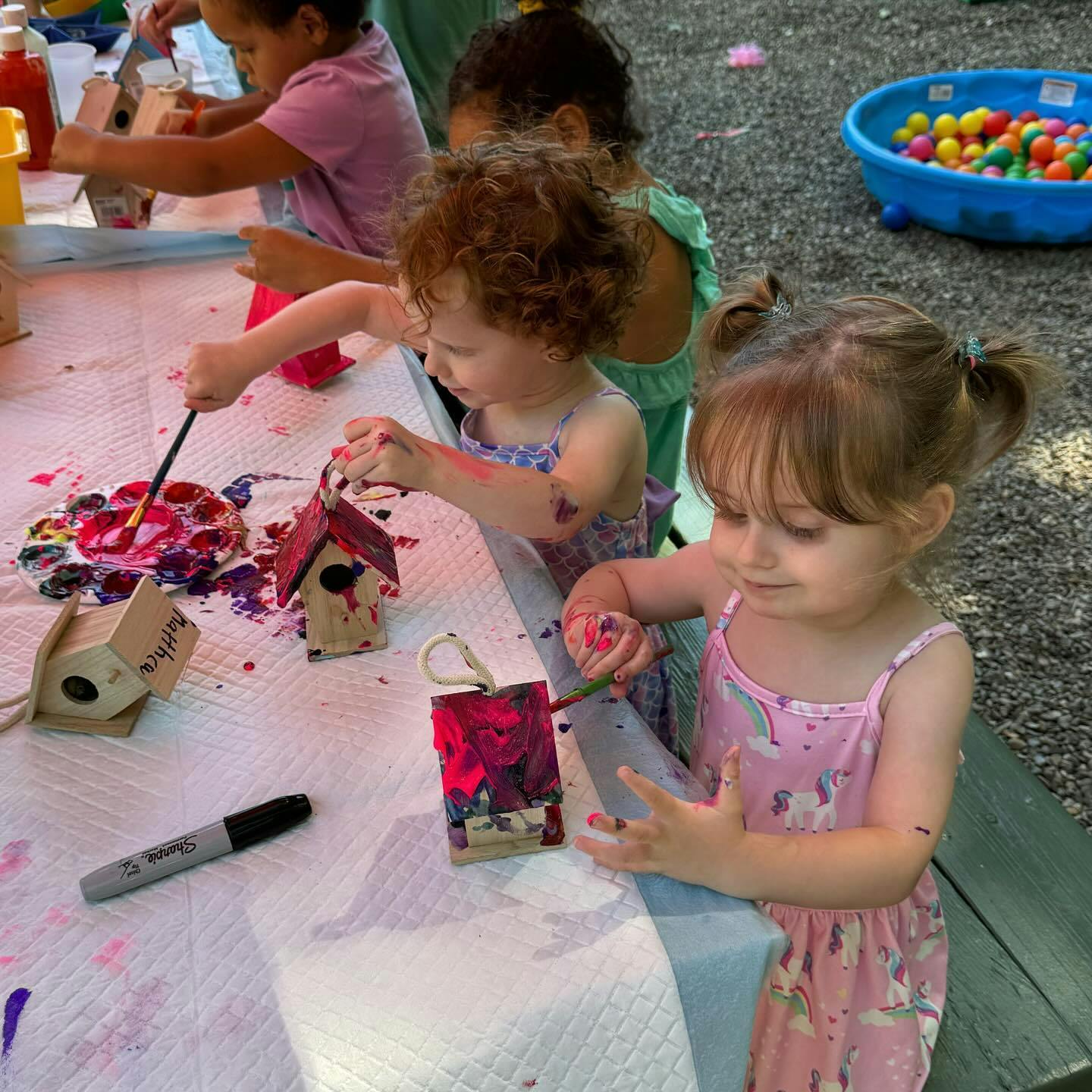 Children painting small birdhouses and other crafts at a table