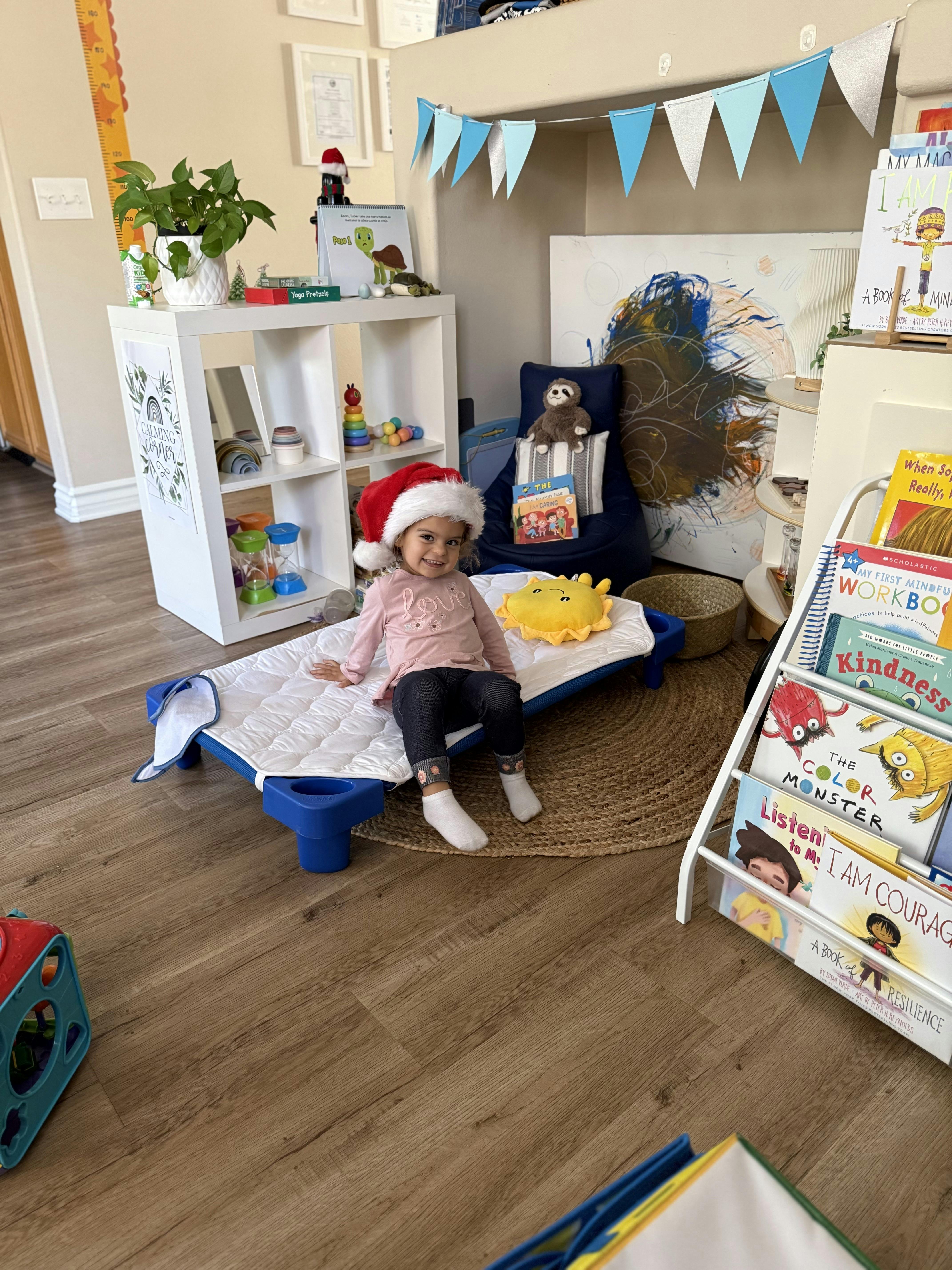 Child wearing a Santa hat sitting on a cot in a play area