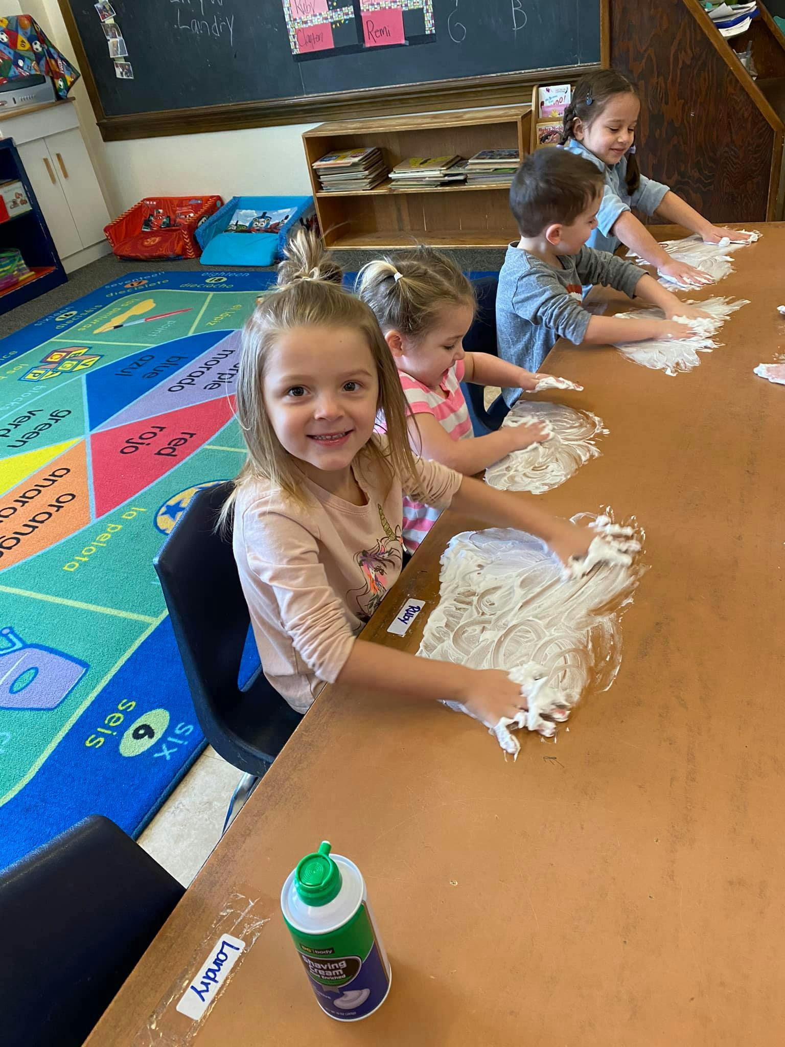 Children playing with shaving cream at a table in a classroom