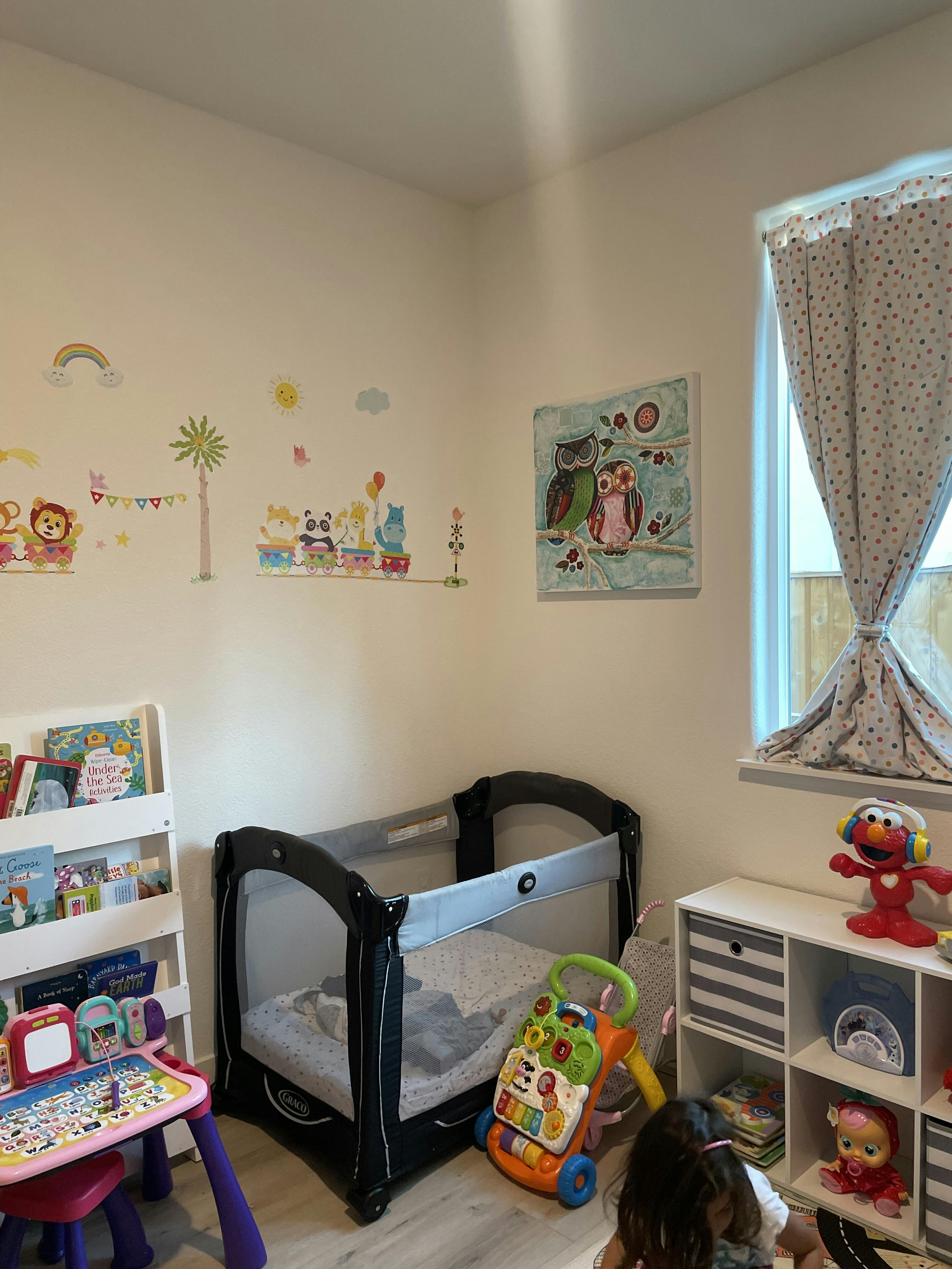 Child's room with a pack-and-play, toys, books, and wall decals