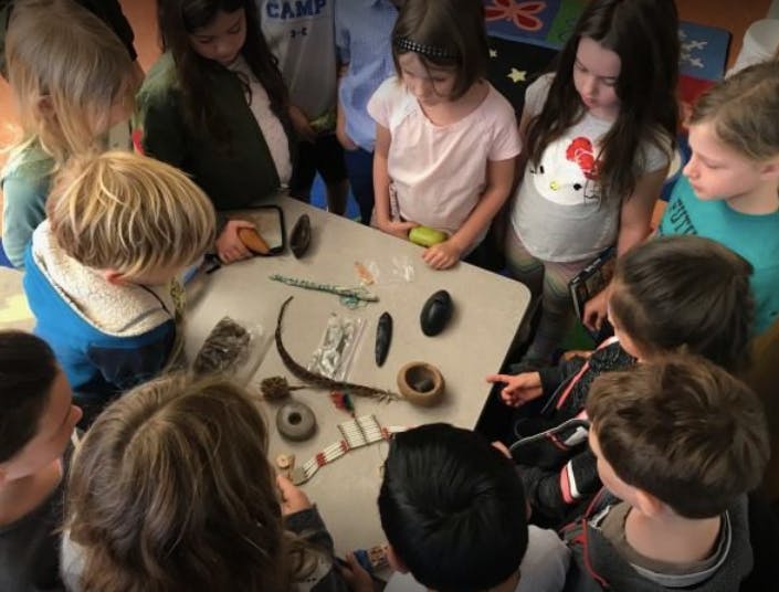 Children gathered around a table looking at various natural objects