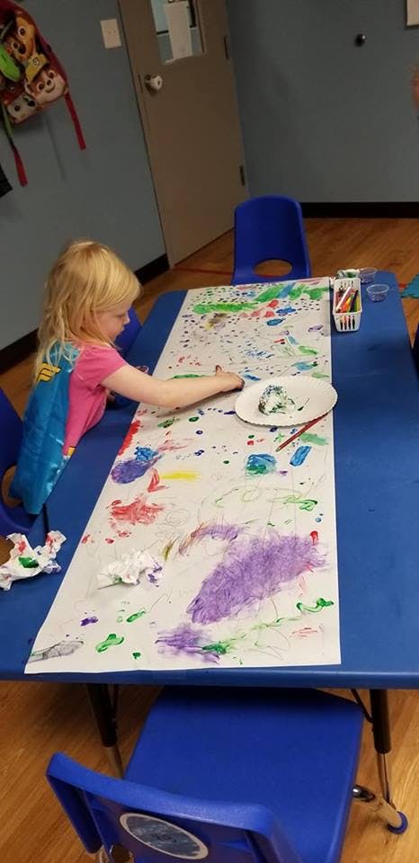 Child painting on a long sheet of paper on a blue table