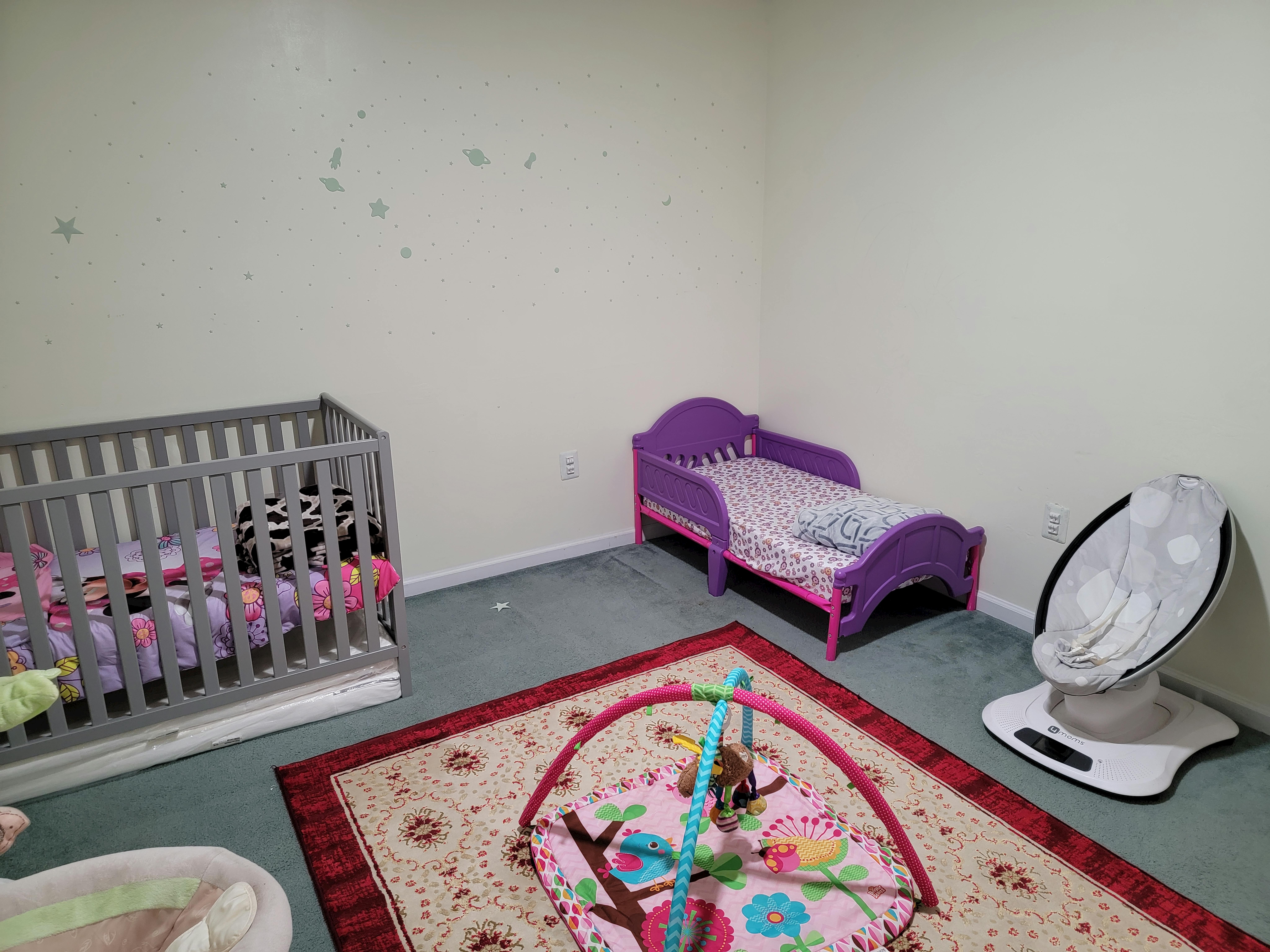 Nursery room with a crib, toddler bed, baby swing, and play mat