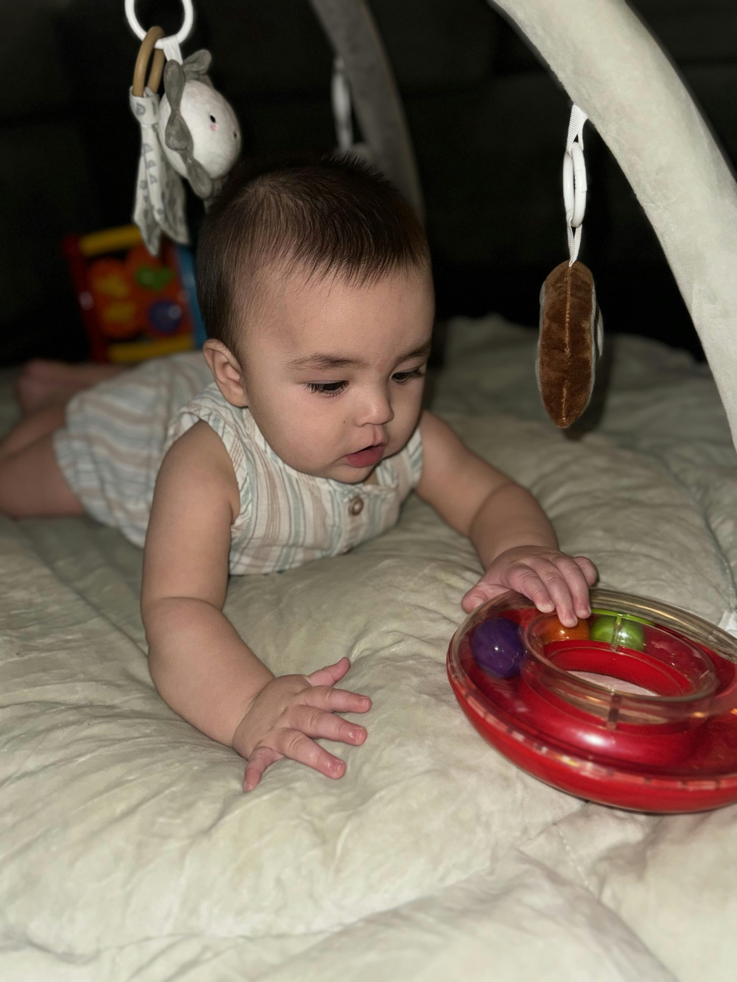 Child on a playmat reaching for a red toy
