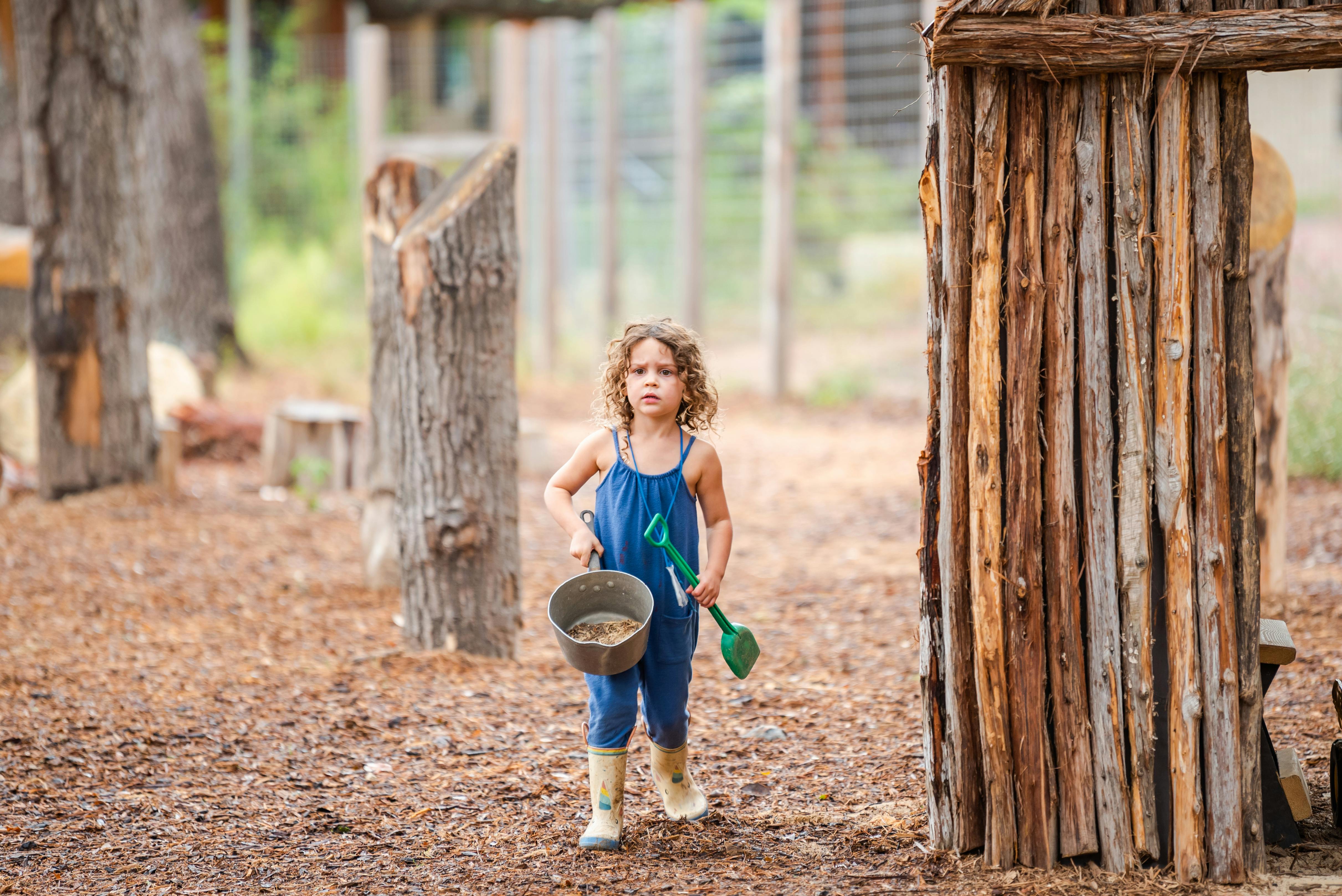 Child in overalls holding a bucket and shovel outdoors