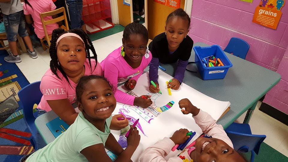 Four children drawing at a table in a classroom