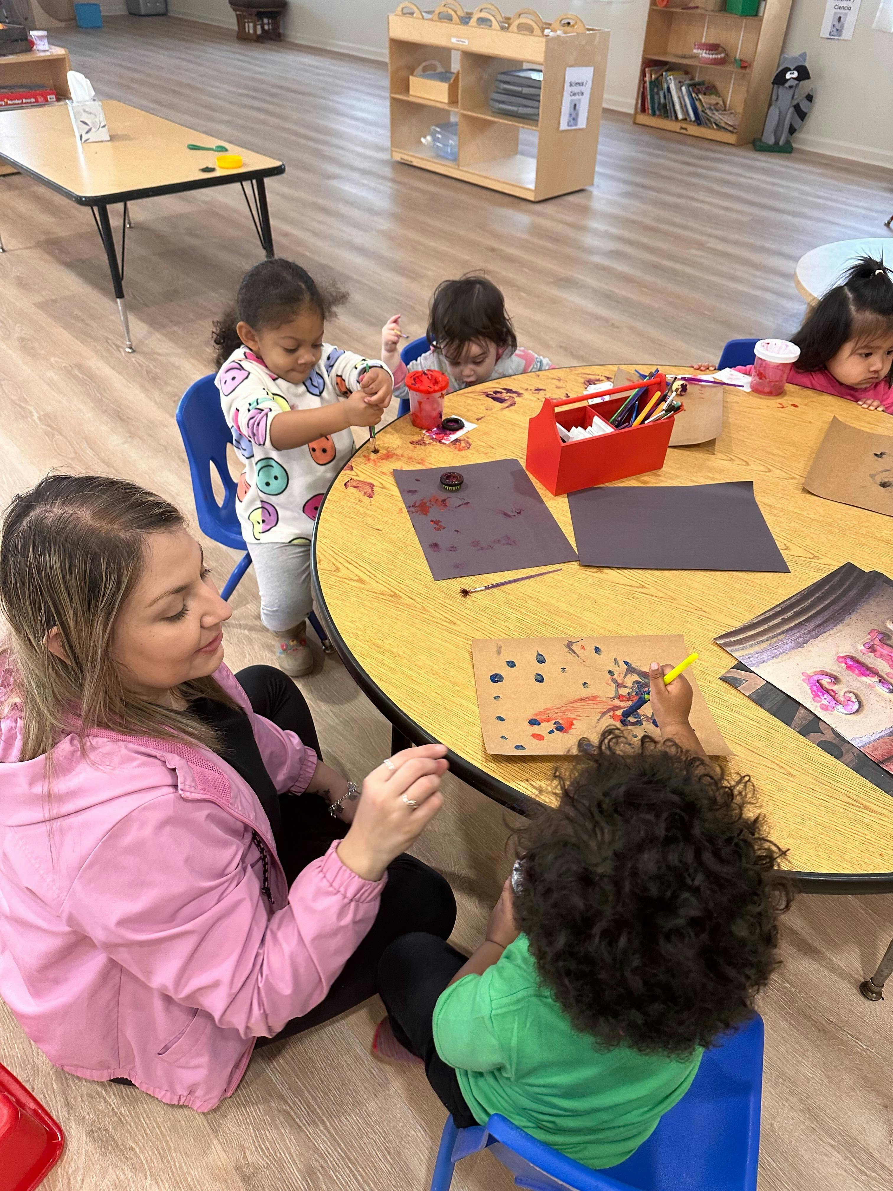 Adult and children painting at a table in a classroom
