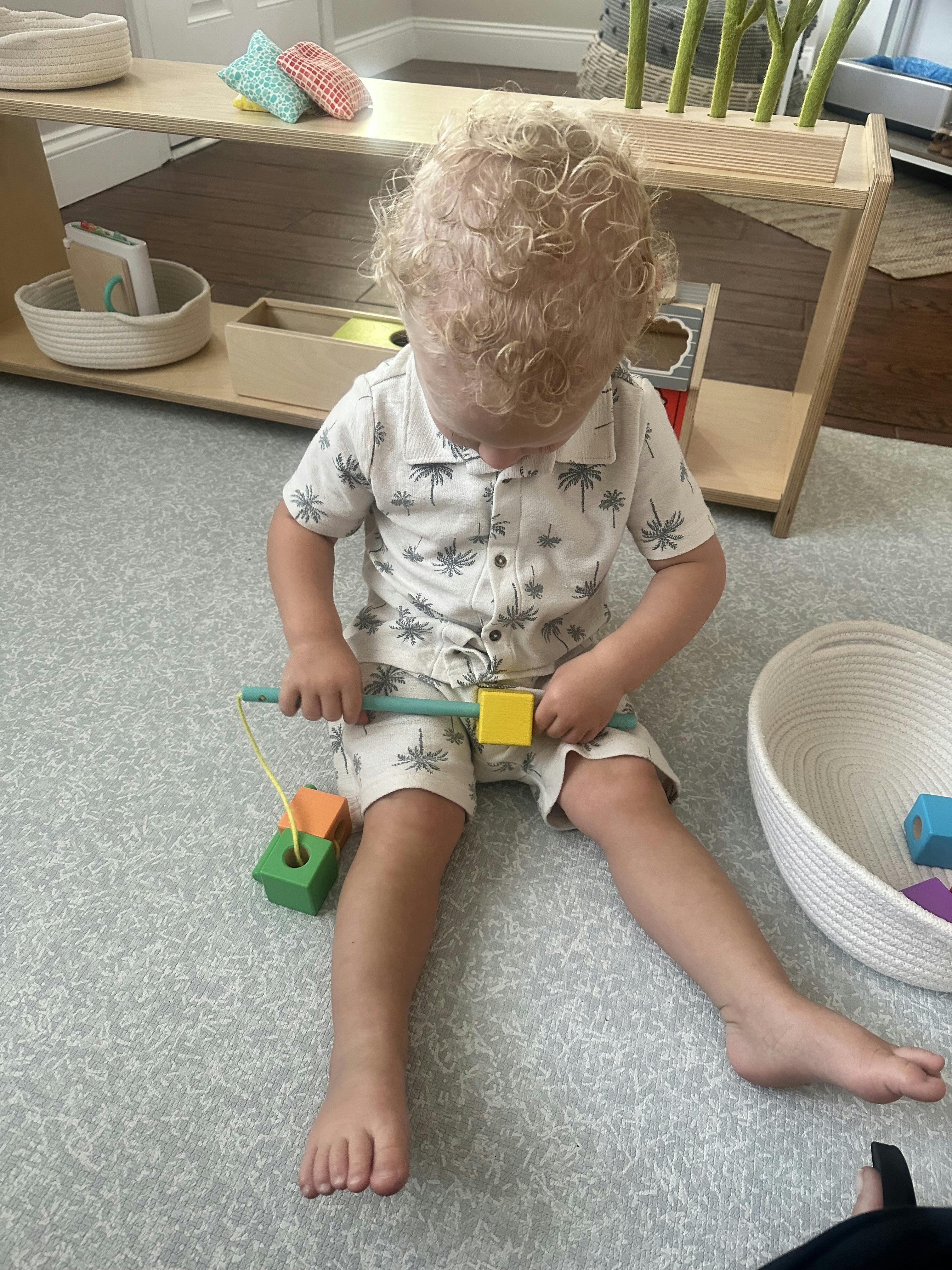 Child sitting on a floor playing with a wooden bead threading toy