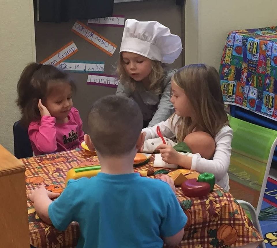 Four children playing at a table, one wearing a chef's hat