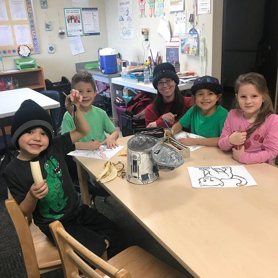 Five children sitting at a table with drawings and bananas