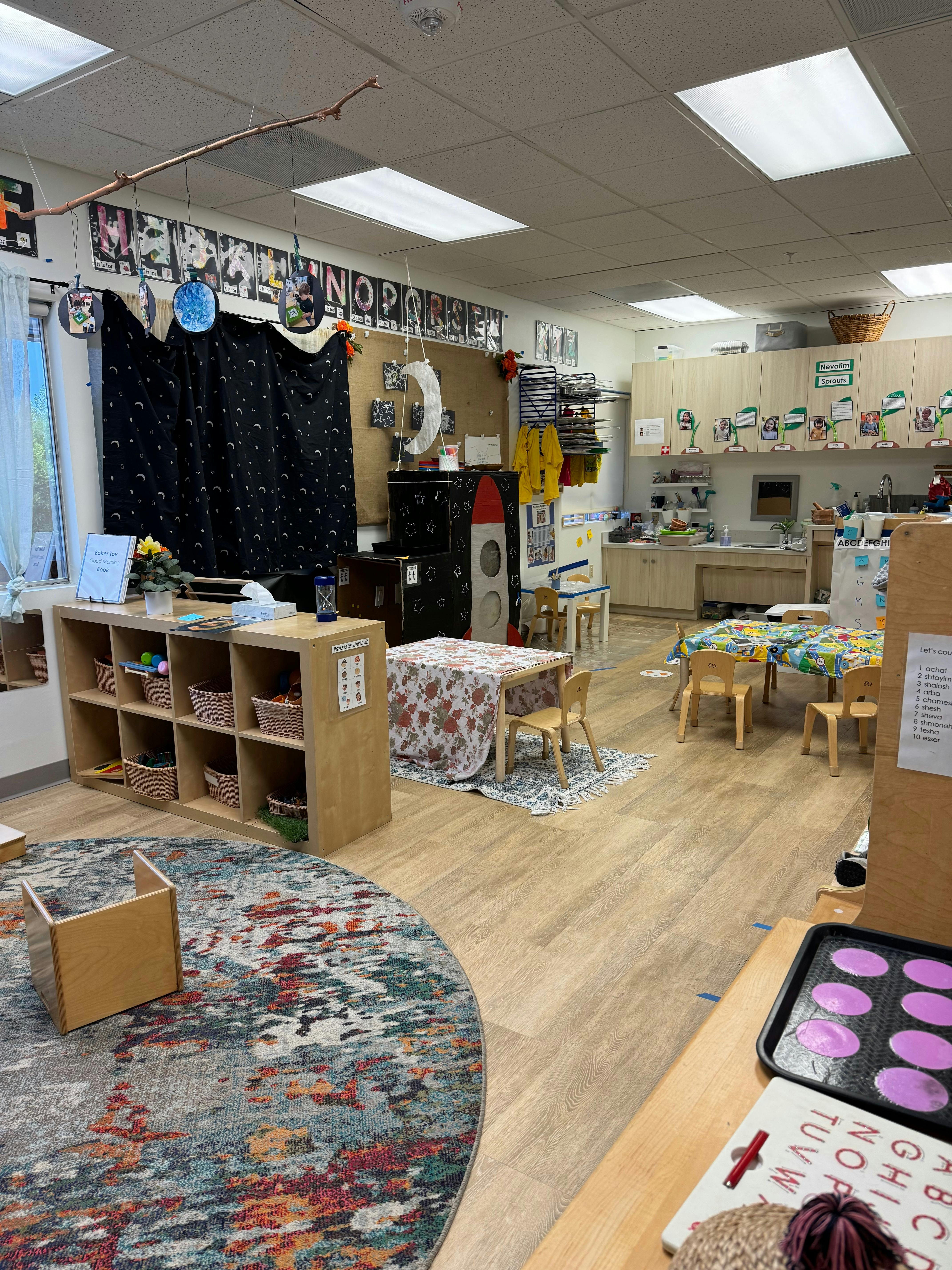 Classroom with small tables and chairs, shelves, and a colorful rug