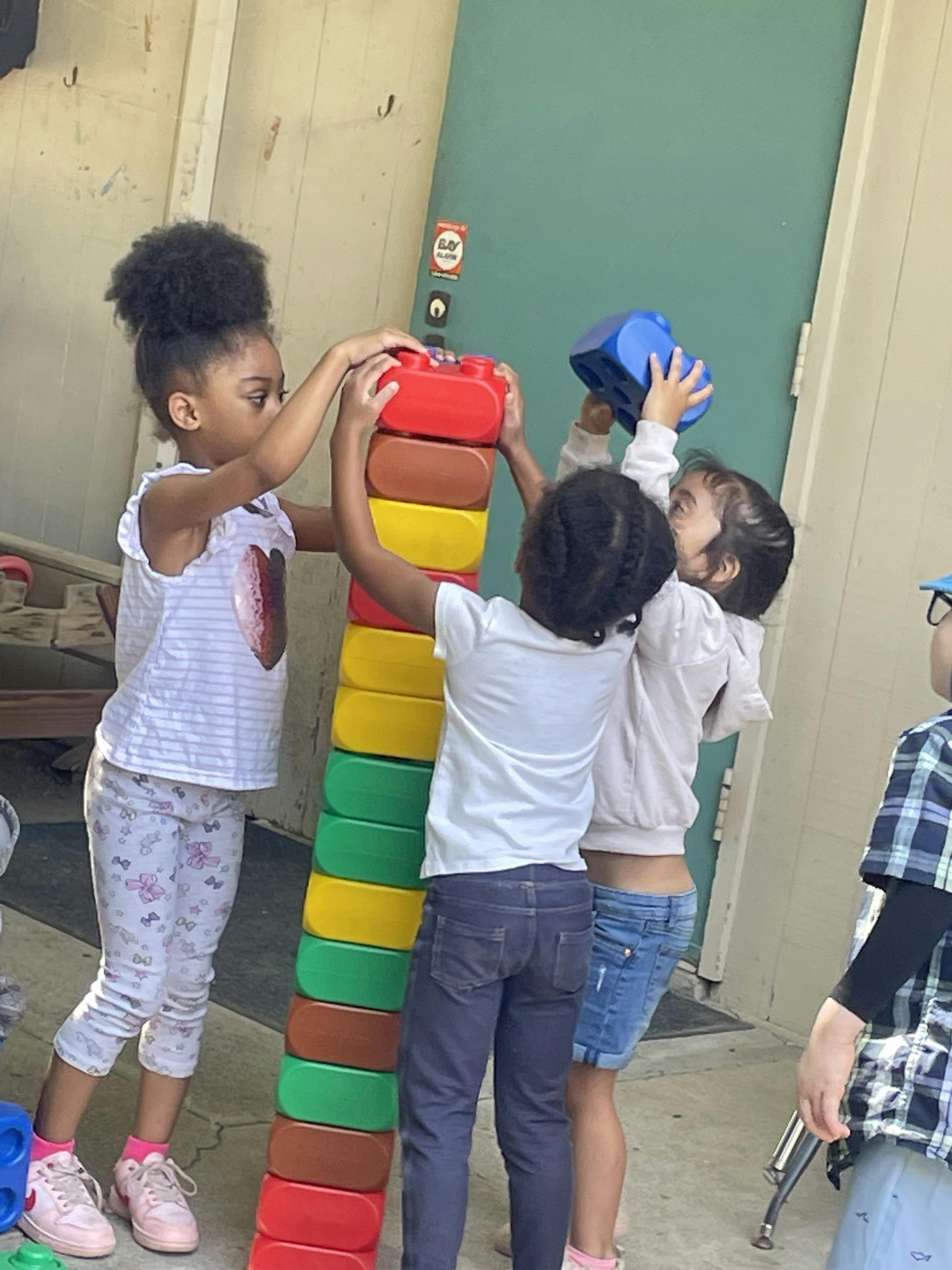 Three children stacking large colorful plastic blocks together