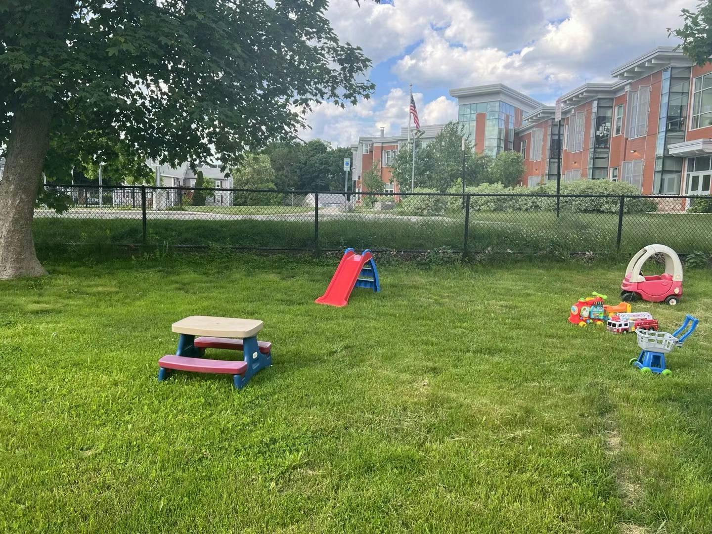 Playground with a small slide, picnic table, and toy car on grass