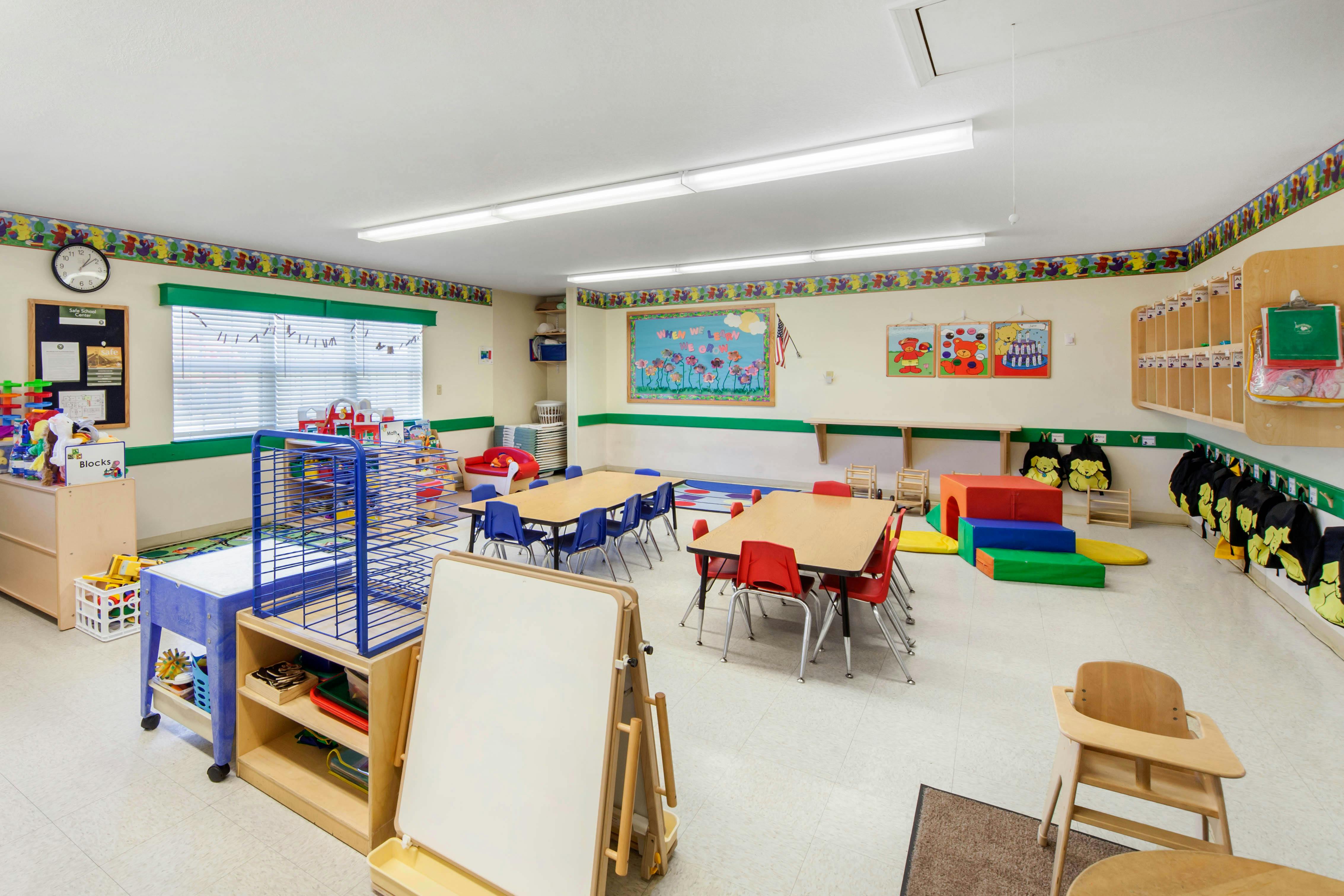 Classroom with child-sized tables and chairs, play mats, and storage shelves