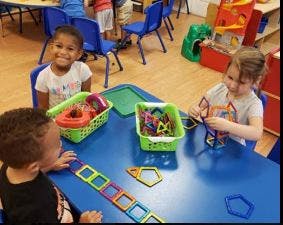Three children playing with magnetic shapes at a table