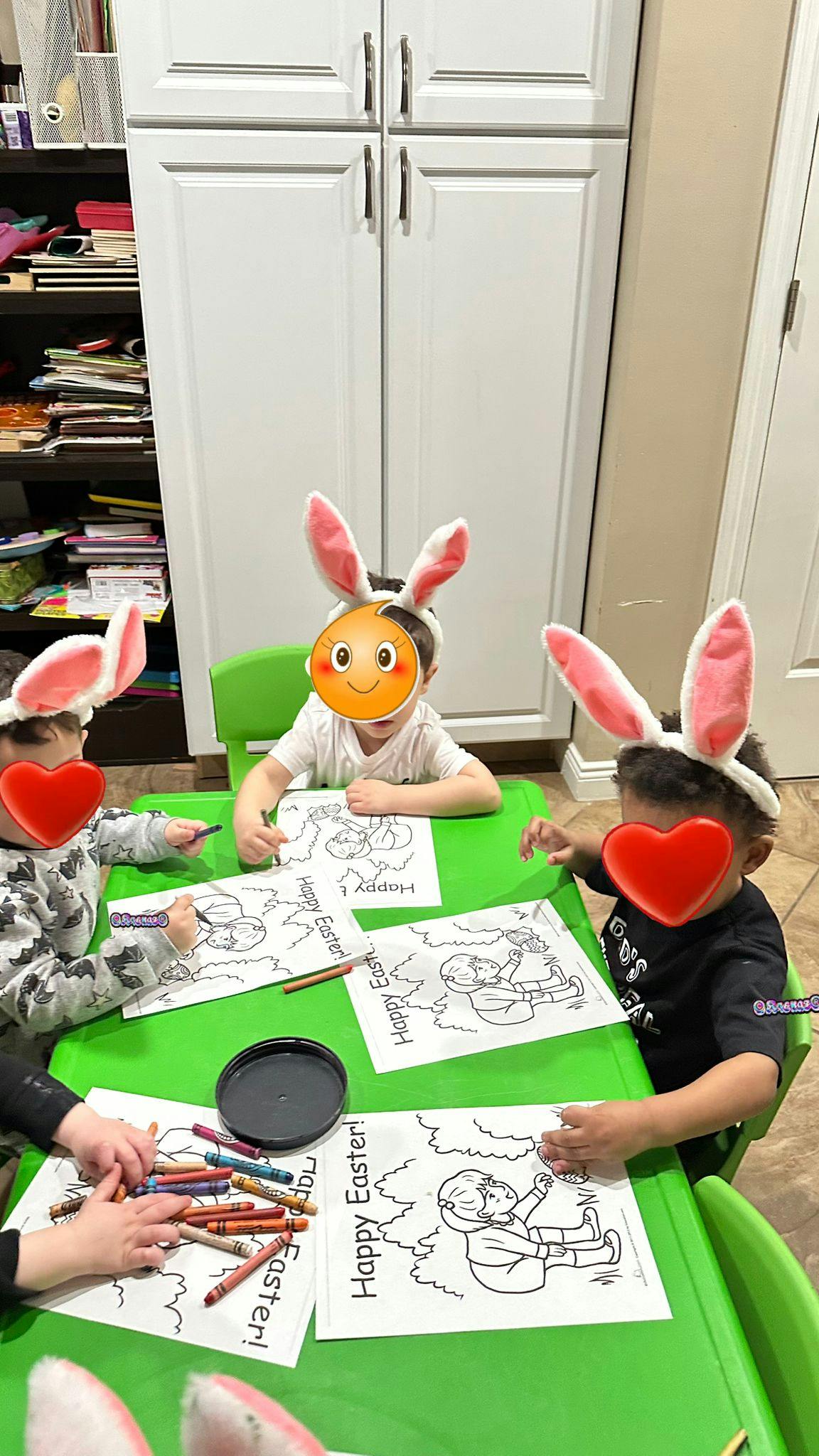 Three children wearing bunny ears coloring at a green table