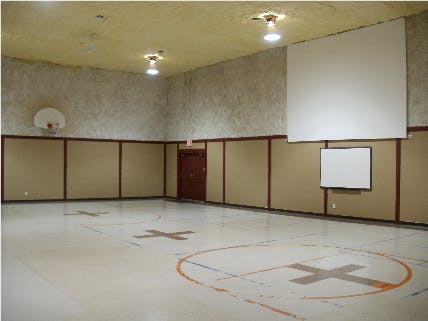 Empty gymnasium with a basketball hoop and projection screen