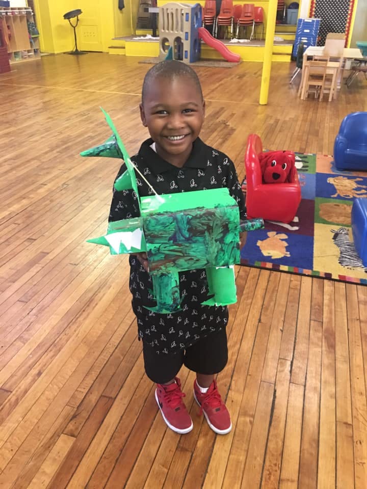 Child holding a green craft project in a classroom