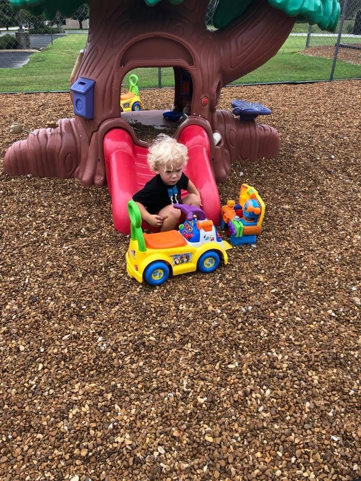 Child sitting on a red slide next to a toy car on a playground