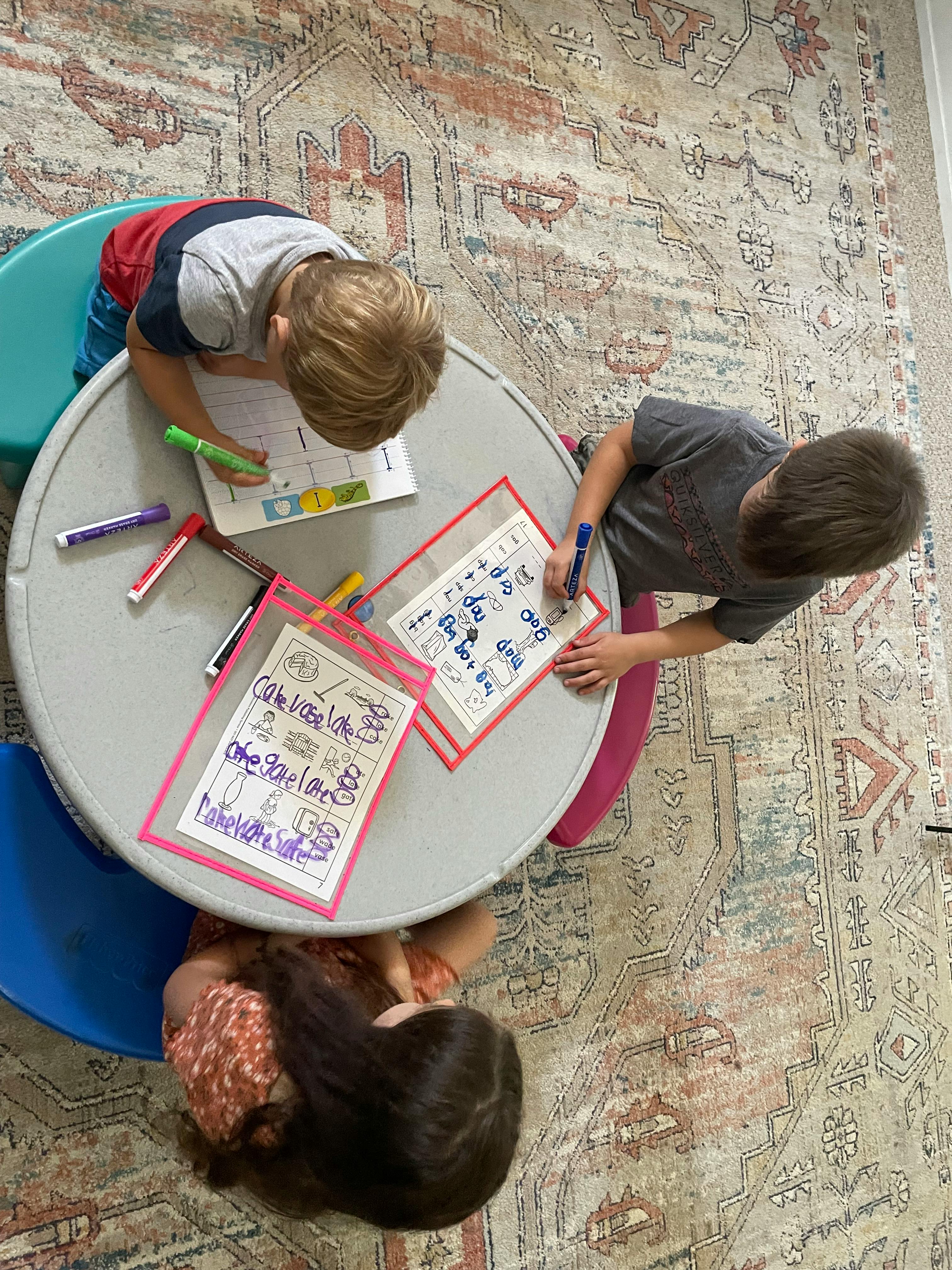 Three children writing and drawing at a round table
