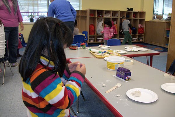Child in striped shirt working with clay at a table in a classroom