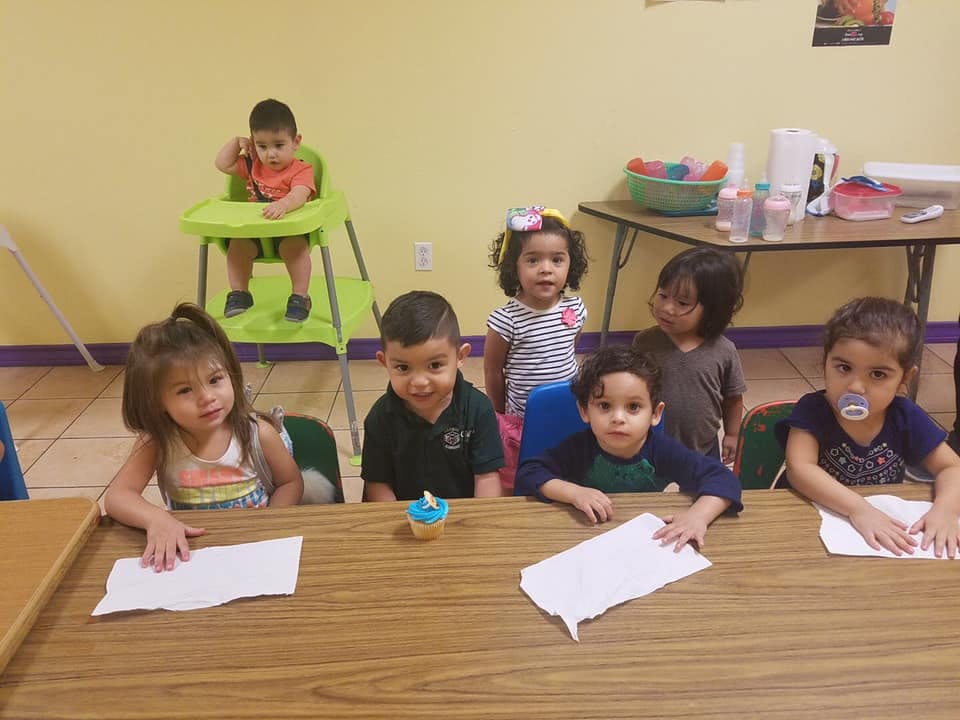 Group of children sitting at a table, one child in a high chair