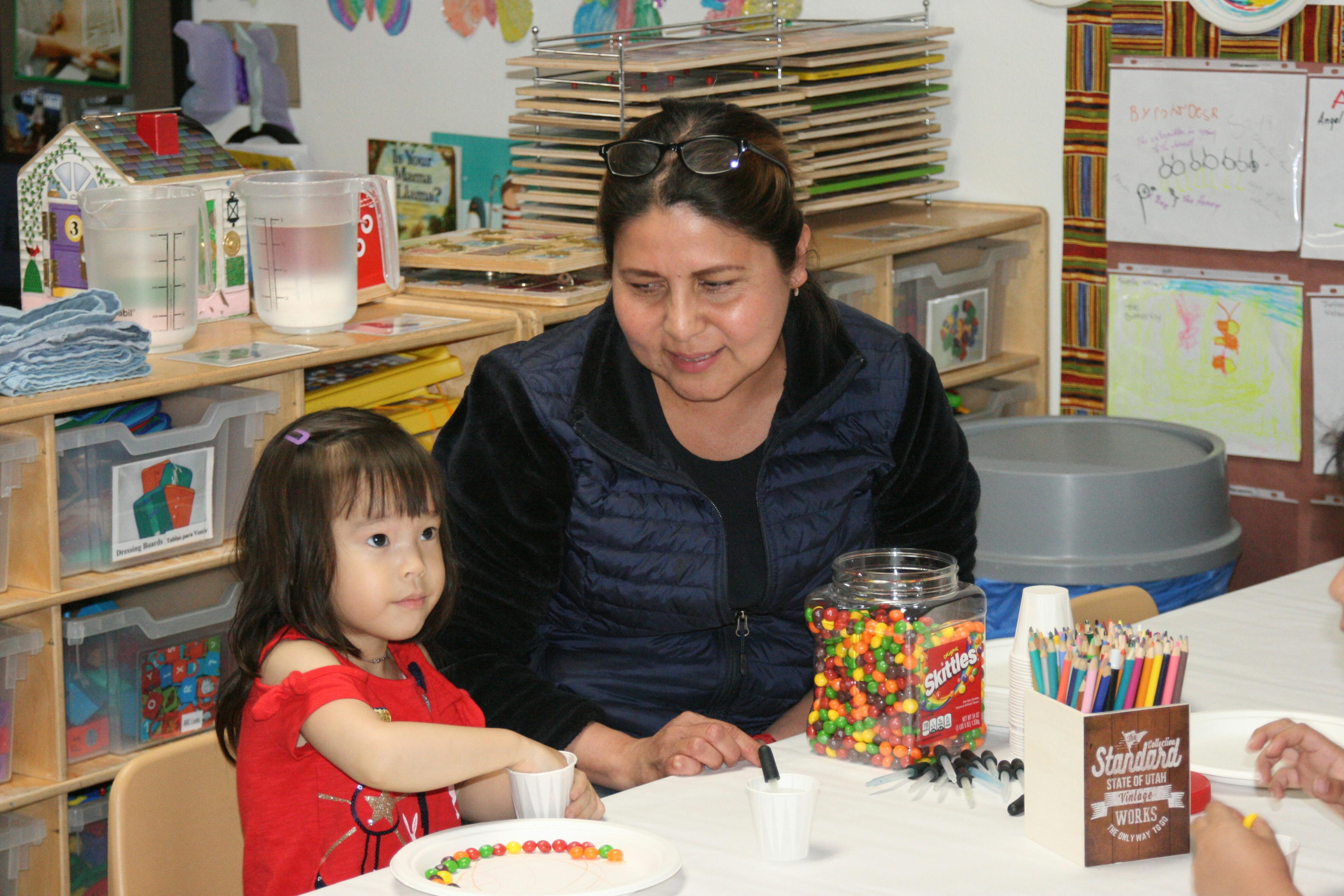 Adult and child at a table with art supplies in a classroom