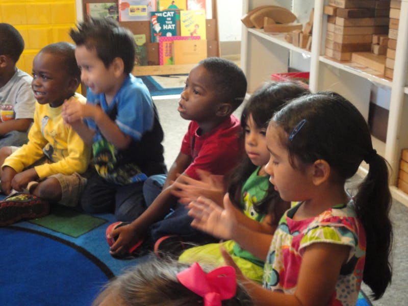 Group of children sitting on the floor, some clapping