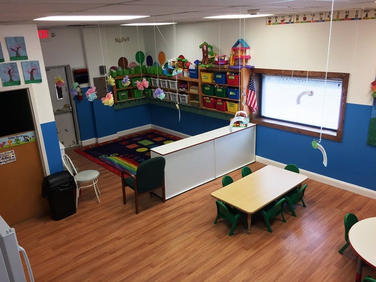A classroom with small tables and chairs, a rug, and shelves with toys