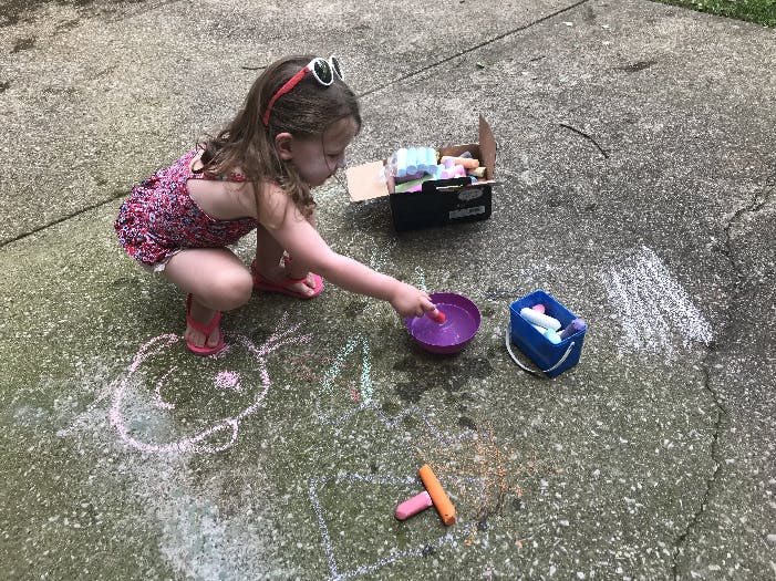 Child playing with chalk and water on pavement