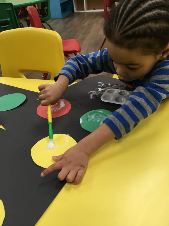 Child painting on a yellow paper circle