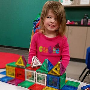 Child standing behind a structure made of colorful magnetic tiles
