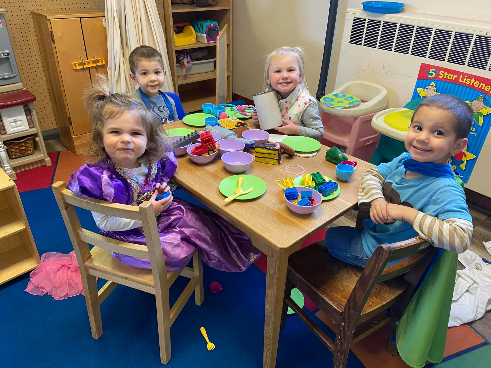 Four children sitting at a table with play dishes
