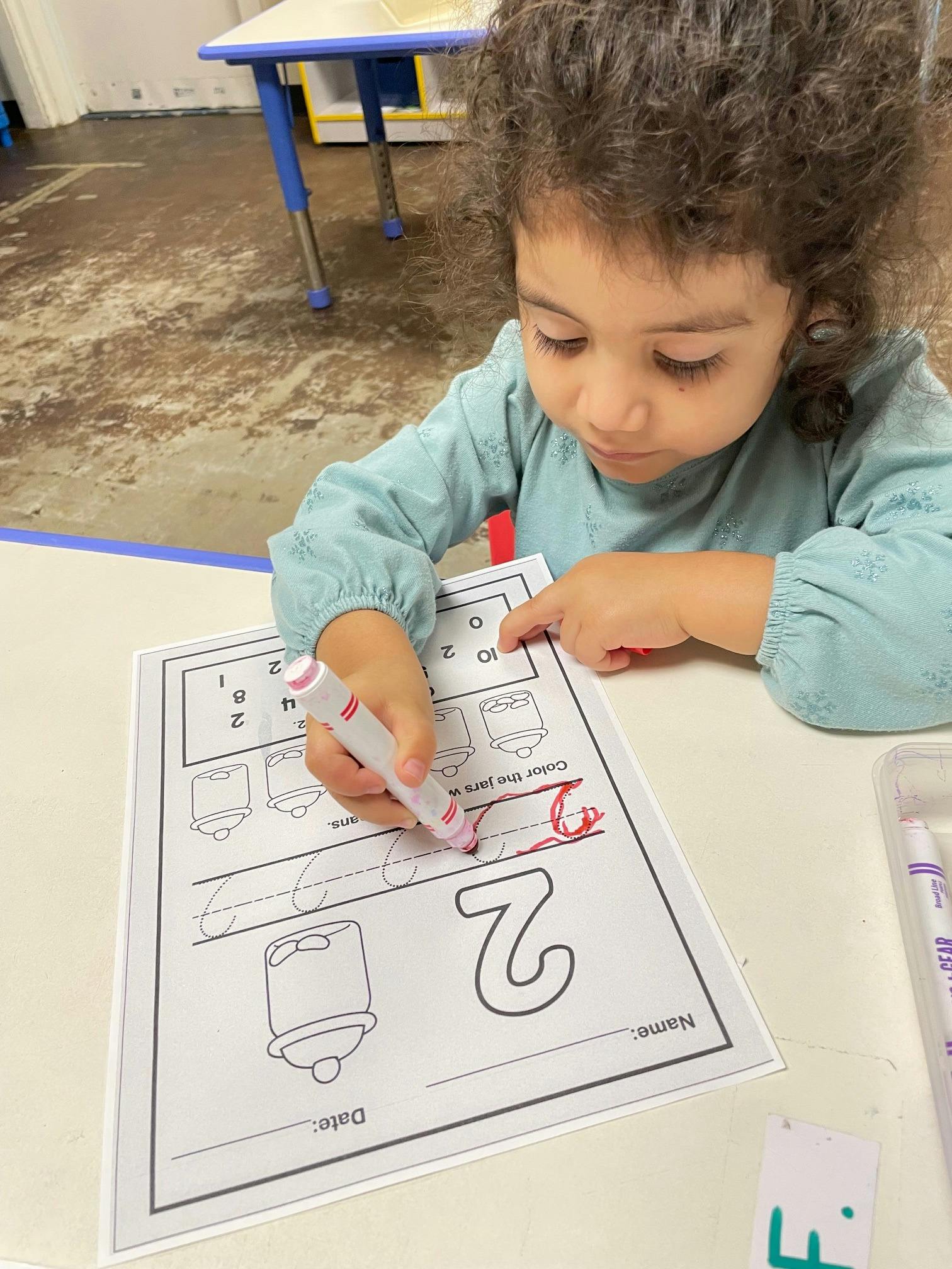 Child writing on a worksheet with a marker