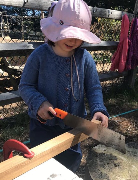 Child in a hat sawing a piece of wood