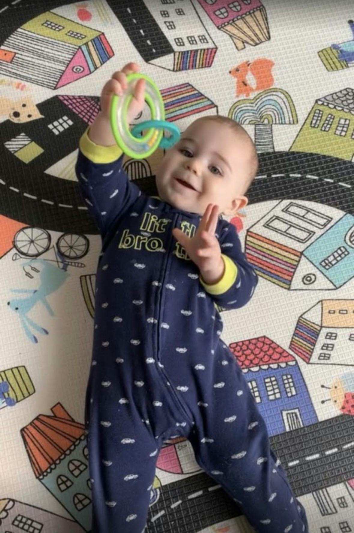 Child in a navy onesie playing with a green and blue rattle