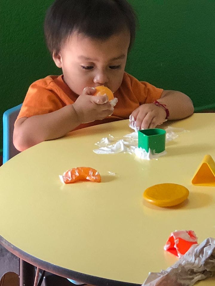 Child eating a piece of fruit at a table