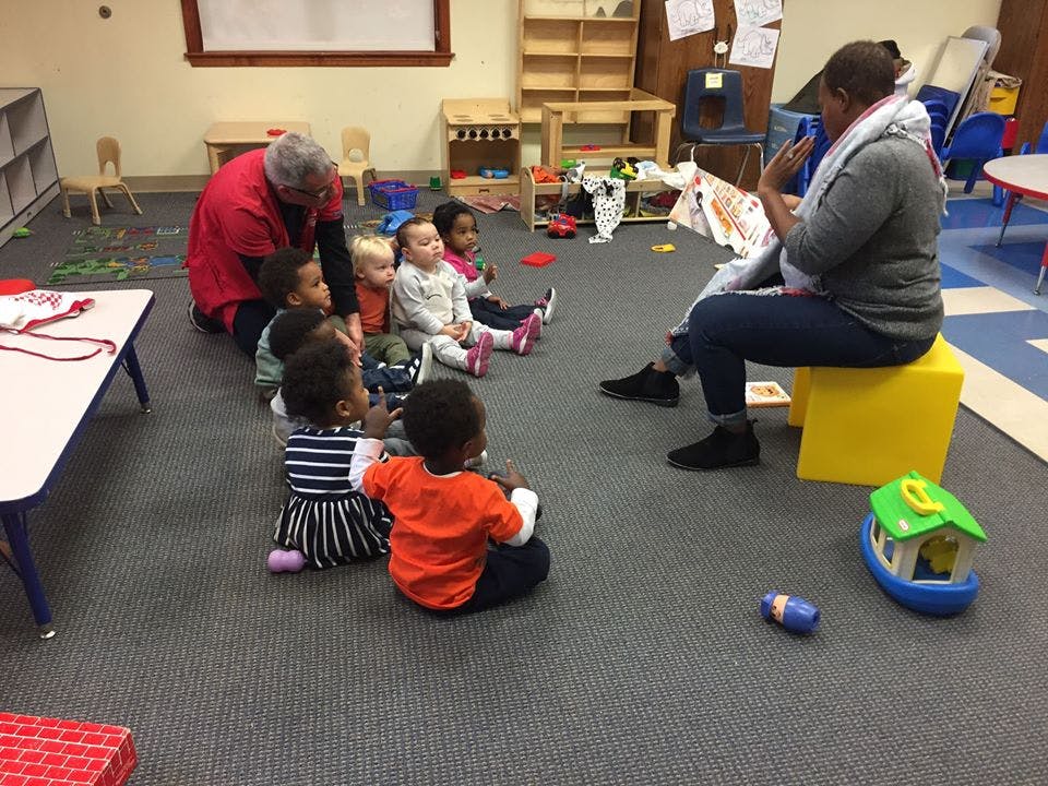Two adults reading to a group of children in a classroom