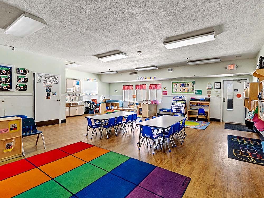 Classroom with small tables and chairs, a colorful rug, and bulletin boards