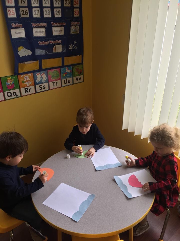 Three children doing crafts at a round table in a classroom
