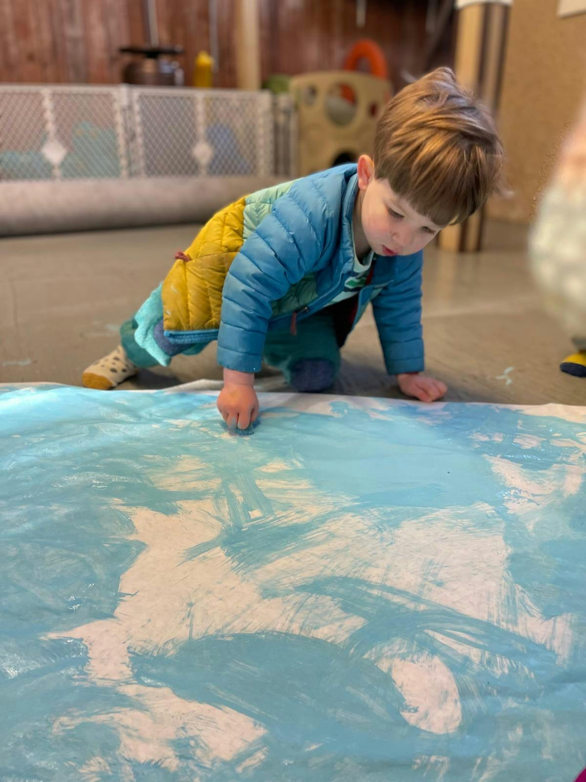 Child on hands and knees painting on a large sheet