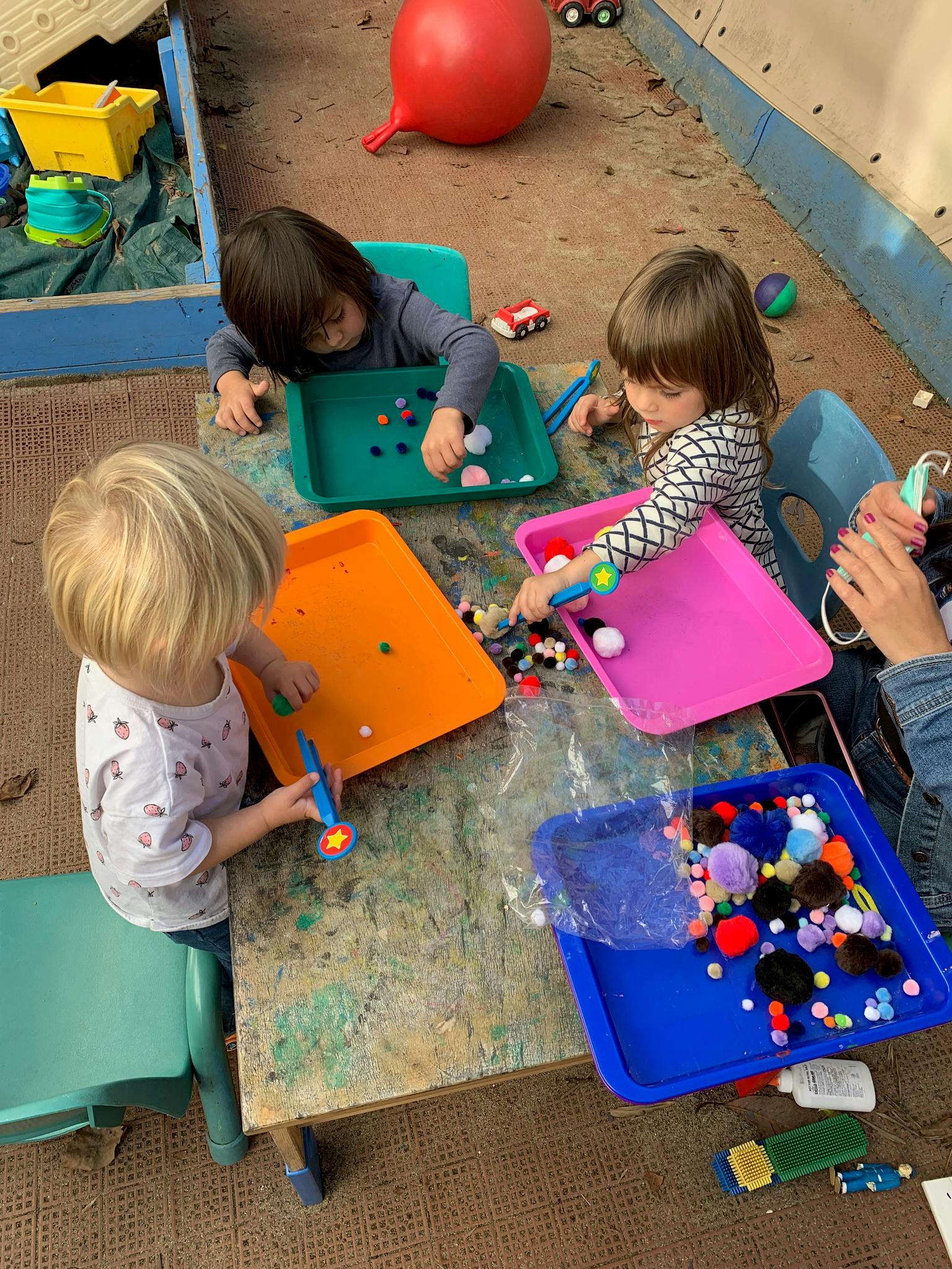 Three children playing with colorful craft supplies at a table