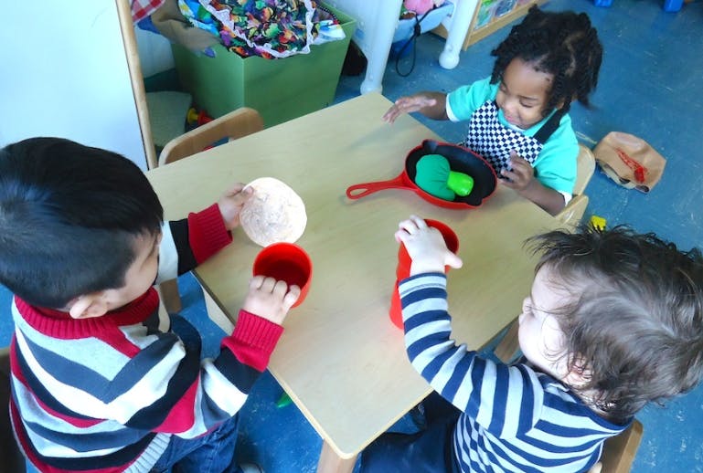 Three children playing with toys at a table in a classroom