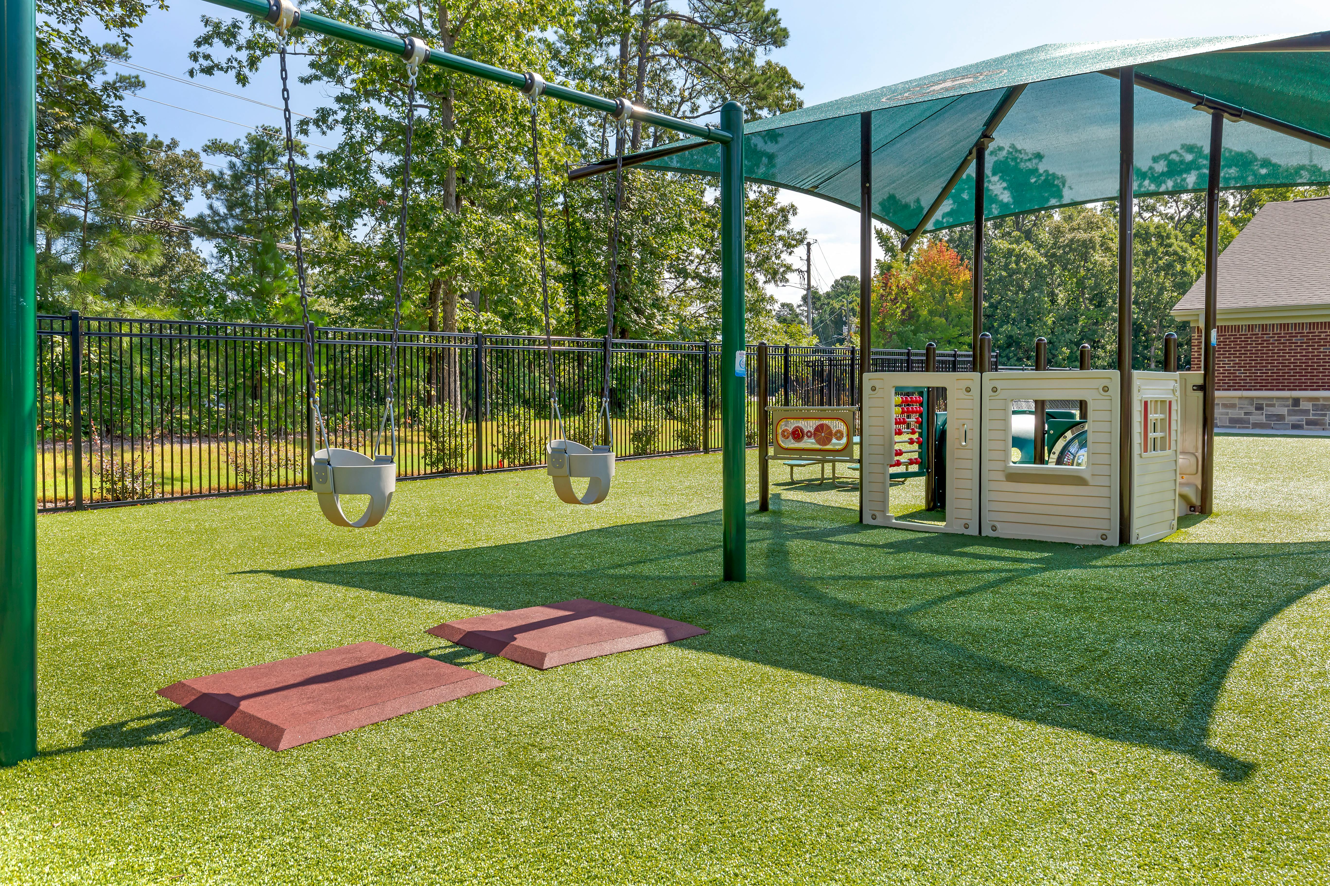 Empty outdoor playground with swings, play structure, and green turf