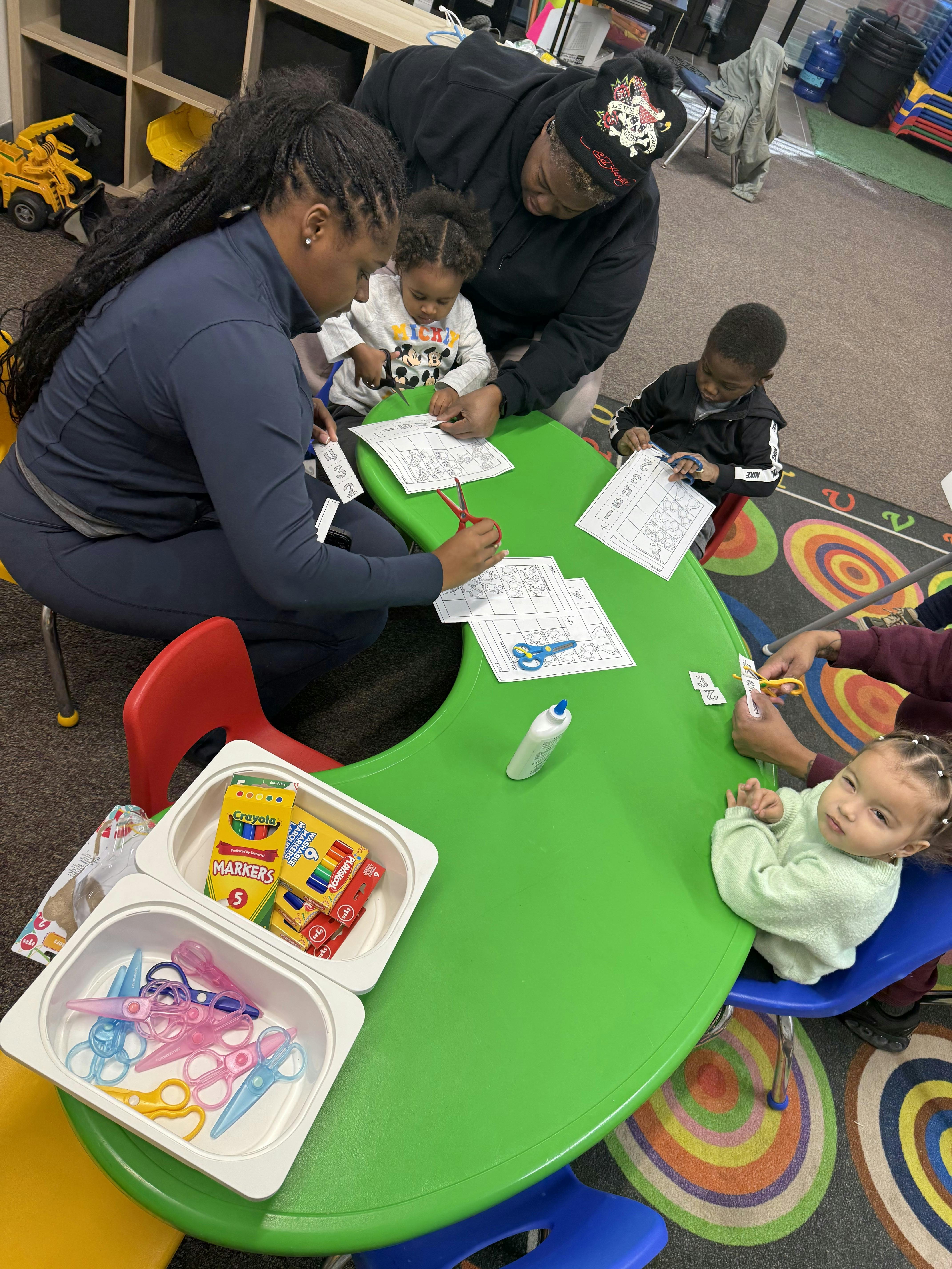 People and children cutting paper with scissors at a green table
