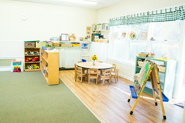 Classroom with small table and chairs, shelves with toys, and an easel